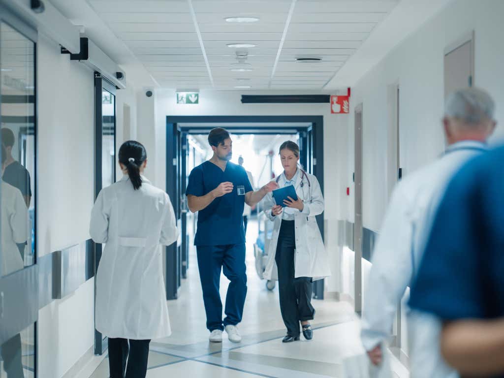Medical staff navigating a busy hospital hallway. Female doctor and male nurse having a discussion.